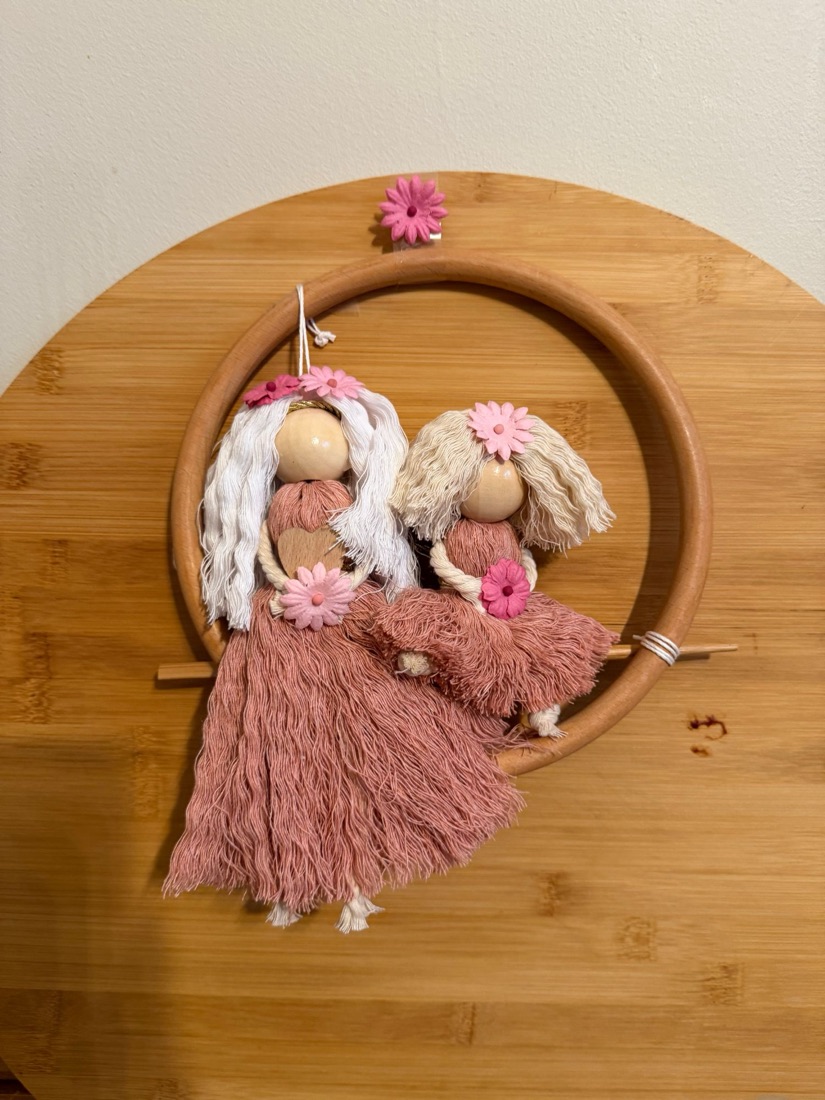 Handmade macramé sister dolls on a swing in a wooden hoop wall hanging